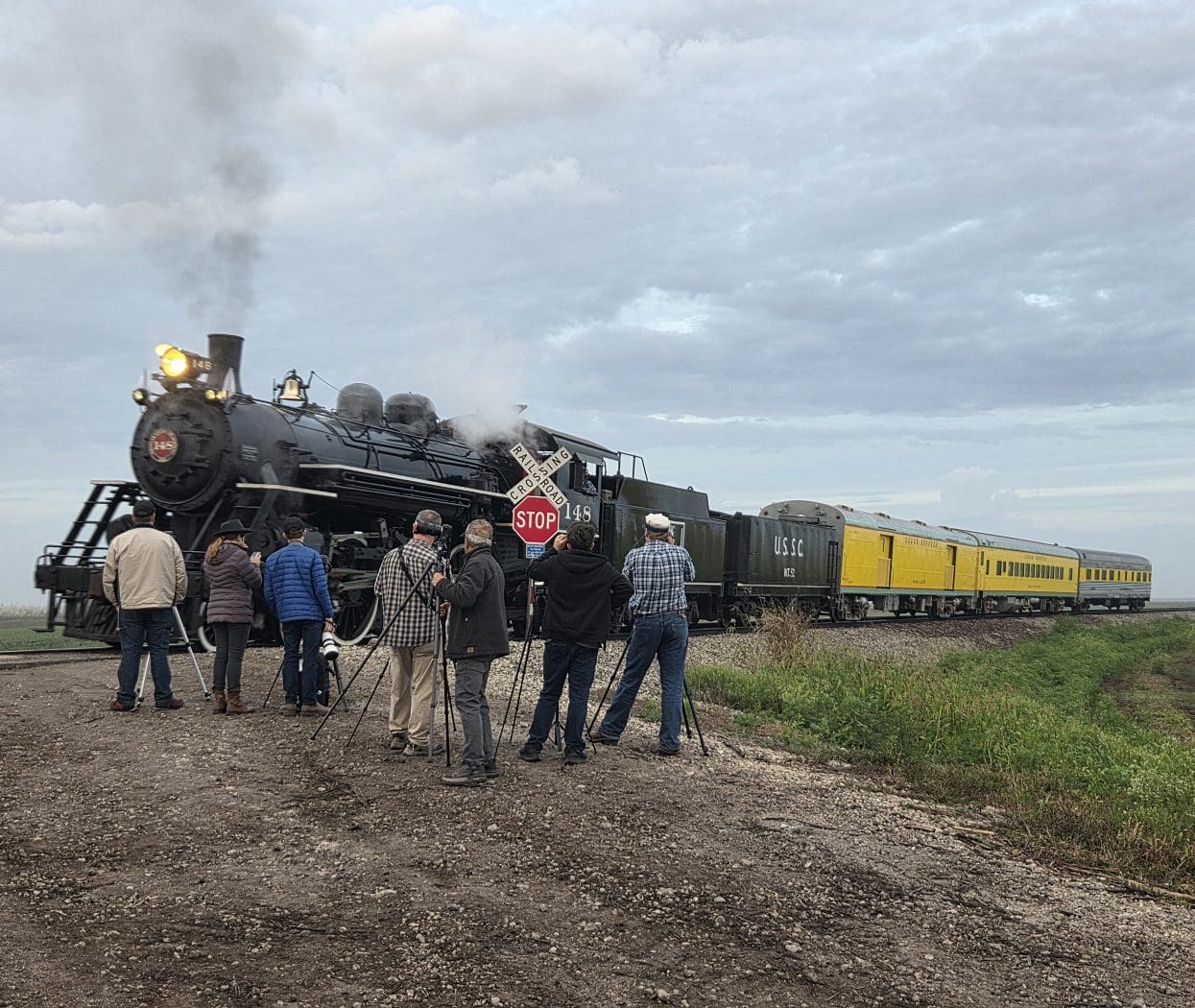 Photographers capturing steam locomotive at railway crossing